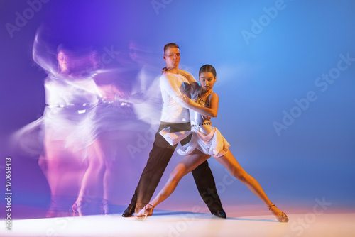 Dynamic portrait of graceful dancers, flexible man and woman dancing ballroom dance isolated on gradient blue purple background in neon mixed light