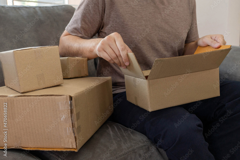 E-commerce concept parcel boxes made by cardboard was assembled with the clear tape by a man sitting on the sofa E-commerce concept parcel boxes made by cardboard was assembled with the clear tape by a man sitting on the sofa
