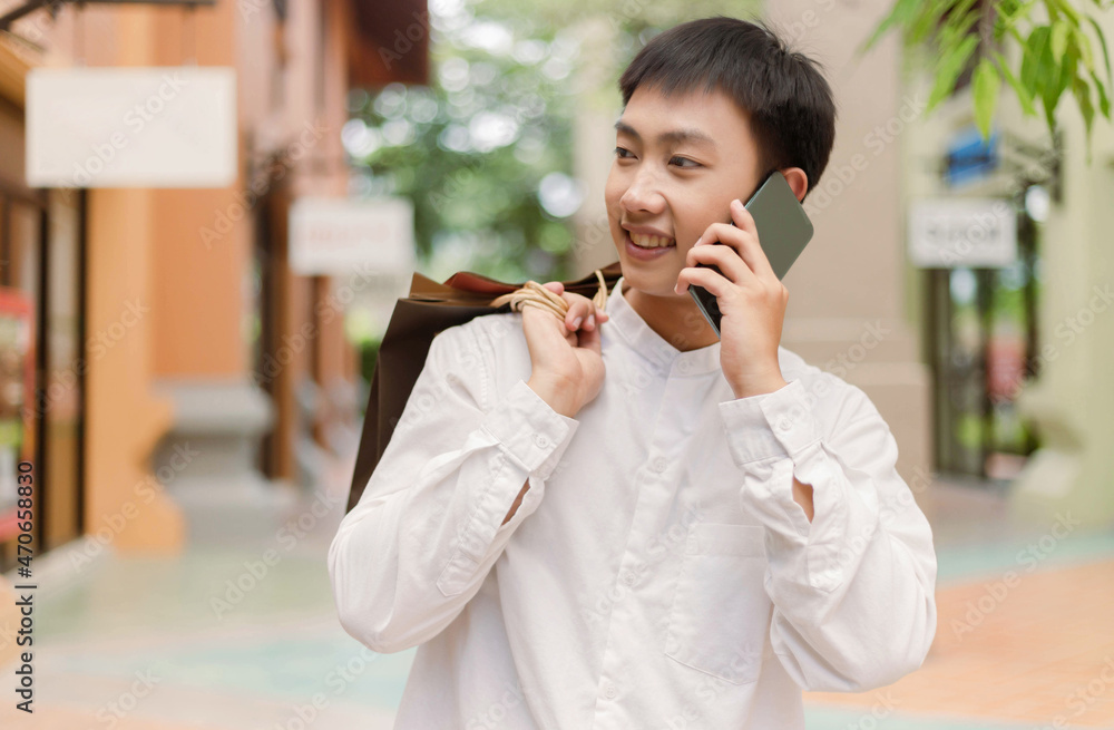Fototapeta premium shopping concept The shopping man who puts shopping bags on his back giving his smile to the shop on his right while having a conversation with someone on the phone