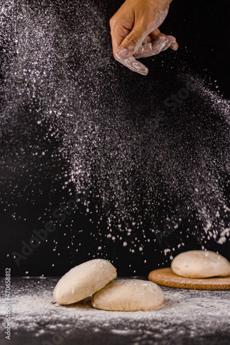 фотографія bread concept a few bun doughs and flour being in the middle on the black backgr