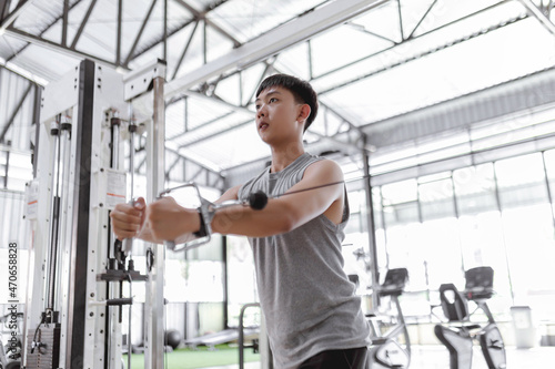 exercise concept The male working out club subscriber standing and giving focus on doing curl pulling the spring rope toward himself together with his both hands