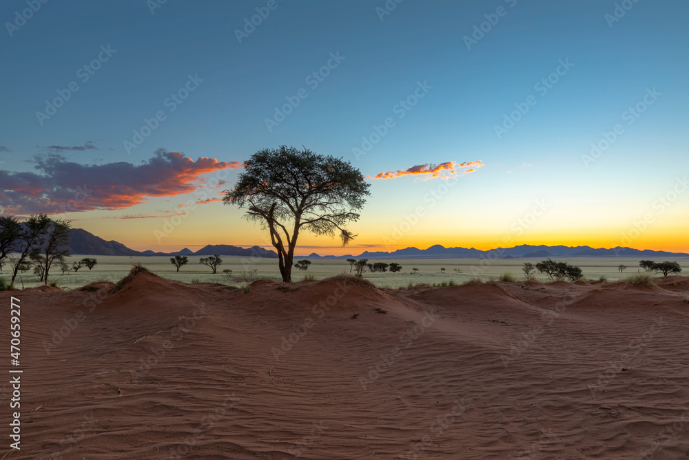 Orange and yellow light on clouds and red sand after sunset in Namib Desert