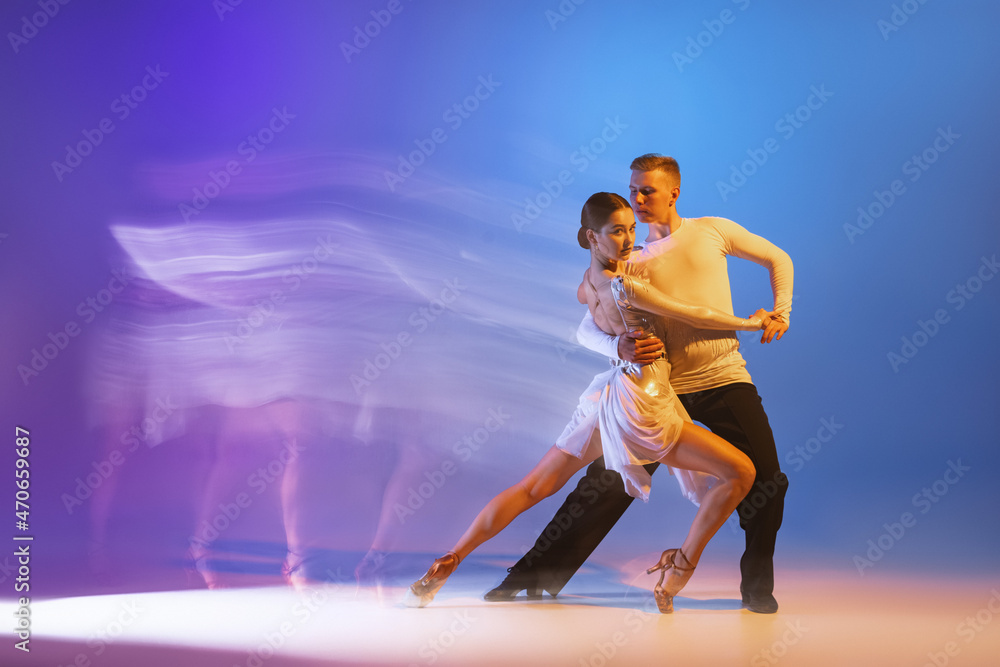 Young graceful dancers, flexible man and woman dancing ballroom dance isolated on gradient blue purple background in neon mixed light
