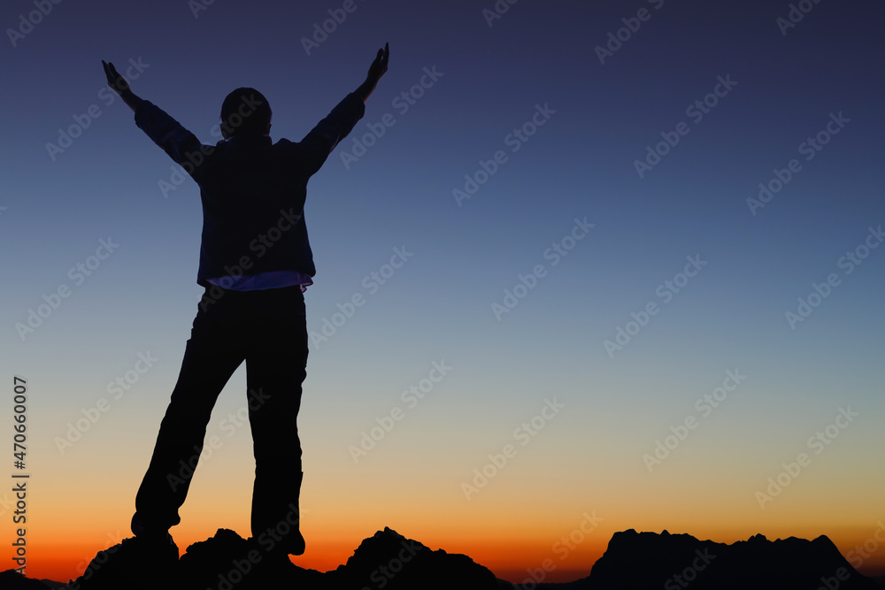 Silhouette success person raised hands on the peak of mountain with Smooth orange blue gradient of dawn sky.