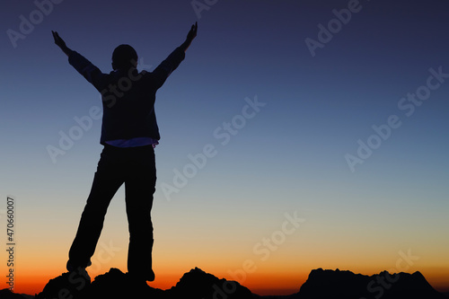 Silhouette success person raised hands on the peak of mountain with Smooth orange blue gradient of dawn sky.