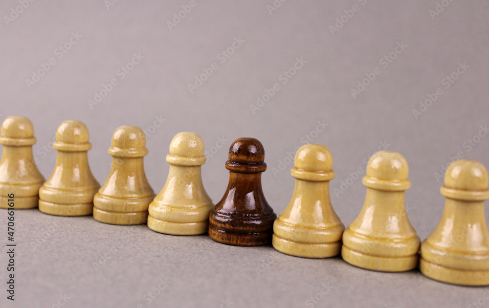 One black chess pawn among whites pawns on gray background. The concept of racism One black chess pawn among whites pawns on gray background. The concept of racism