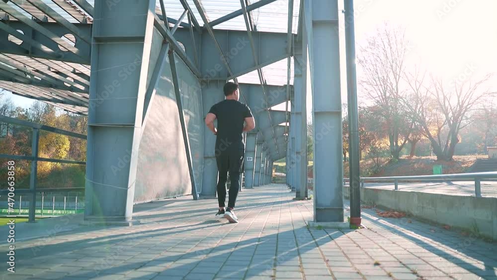 Young asian man runner running down street on urban background of city stadium Rear back view. Morning jog in black sportswear Active healthy lifestyle. Handsome male athlete training cardio jogging Young asian man runner running down street on urban background of city stadium Rear back view. Morning jog in black sportswear Active healthy lifestyle. Handsome male athlete training cardio jogging