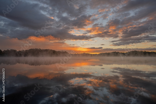 Foggy autumn landscape at dawn of the shoreline of Whitford Lake with mirrored reflections in calm water, Fort Custer State Park, Michigan, USA