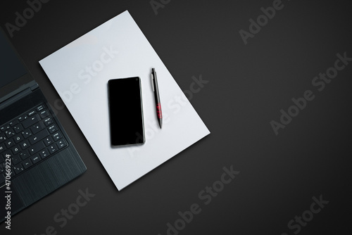 laptop on a dark desk with paper smartphone and pen