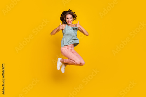 Full body photo of cheerful young happy woman jump up show thumb-up cool isolated on yellow color background © deagreez