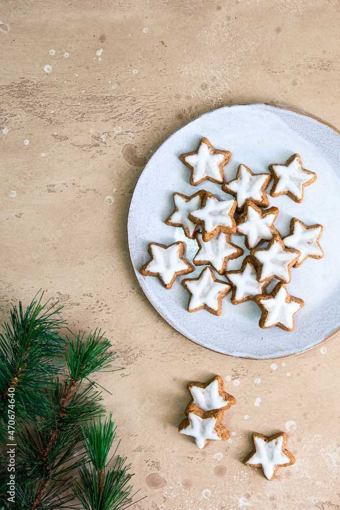 Homemade star shape ginger cookies with sugar icing on white plate on beige bckground with Christmas tree.