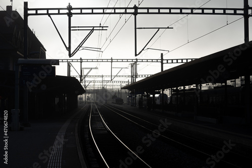 Brouillard dans la gare de Romont en Suisse, photo en contre jour avec les voies et les poteaux.