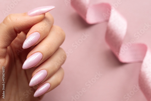 Female hand with a light pink long nails on a light pink background decorated by pink ribbon