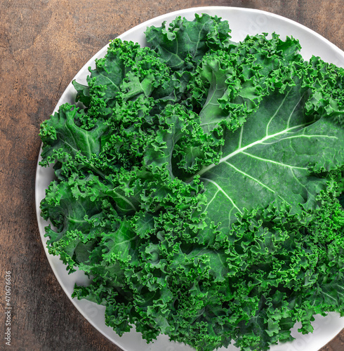 Kale Salad. Fresh Green Kale vegetable leaves on white plate over wooden background, top view. Healthy eating vegetarian food concept..