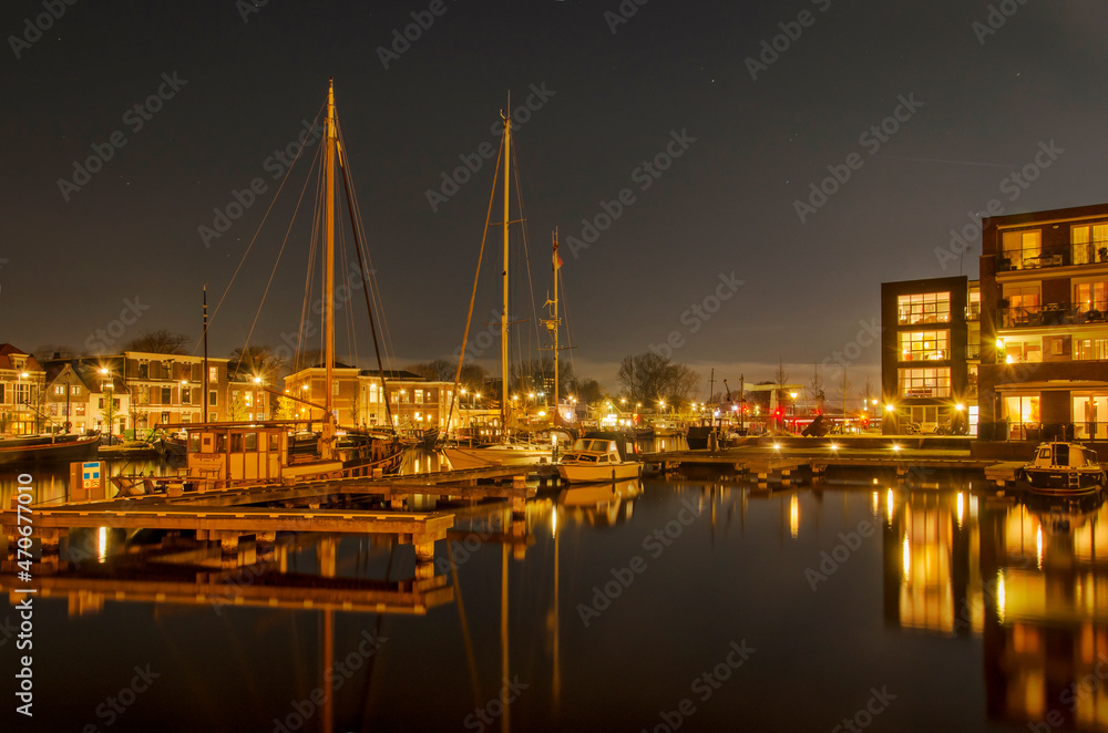 Haarlem, The Netherlands, November 19, 2021: night view of the river Spaarne, with a jetty and sailboats next to a new residential neighbourhood
