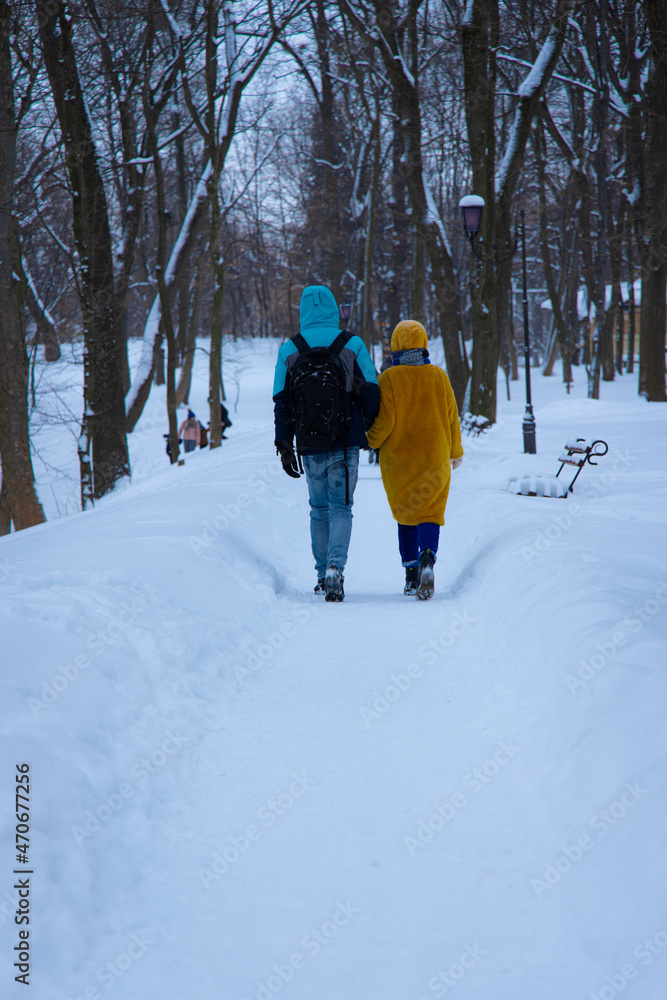 December winter park with a lot of snow, ordinary outdoor view, two person boy and girl walking with holding hands back to camera, vertical photo
