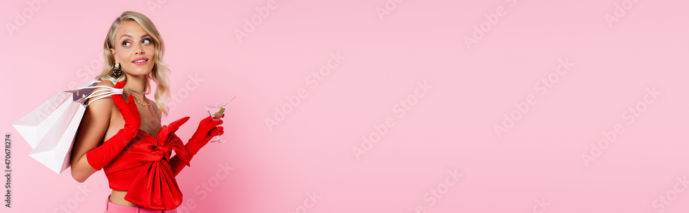 elegant blonde woman in red blouse with bare shoulders holding cocktail and shopping bags isolated on pink, banner elegant blonde woman in red blouse with bare shoulders holding cocktail and shopping bags isolated on pink, banner