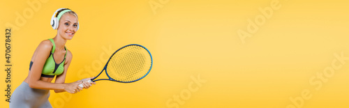 smiling sportswoman in headphones playing tennis isolated on yellow, banner