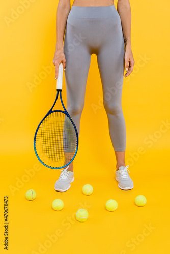 partial view of sportswoman in grey leggings holding racquet while standing near tennis balls on yellow © LIGHTFIELD STUDIOS