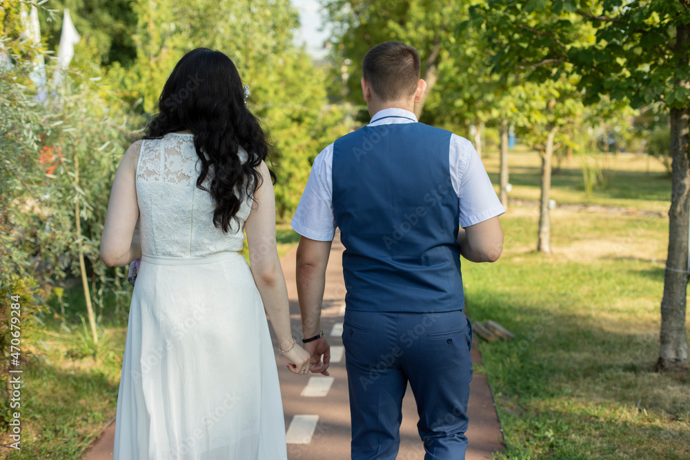 The newlyweds walk along the park path holding hands. The newlyweds walk along the park path holding hands.