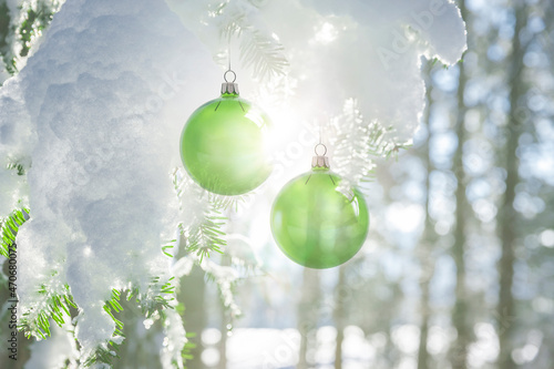 Zwei grüne Weihanchtskugeln an einem schneebedeckten Tannenzweig