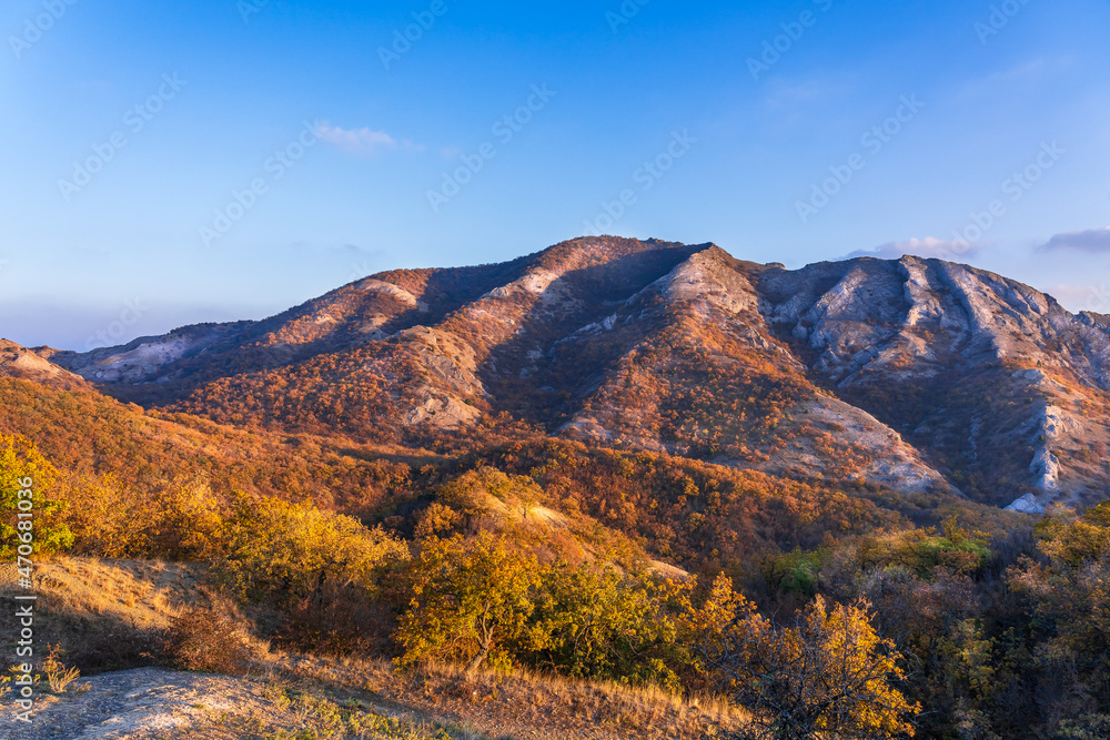 Mountains of white stone covered with autumn forest with yellow leaves illuminated by the sun at sunset from the side. Beautiful play of light and shadow