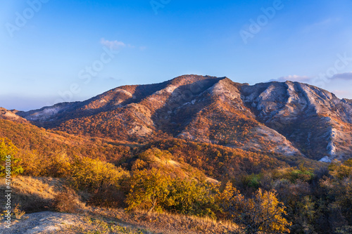 Mountains of white stone covered with autumn forest with yellow leaves illuminated by the sun at sunset from the side. Beautiful play of light and shadow