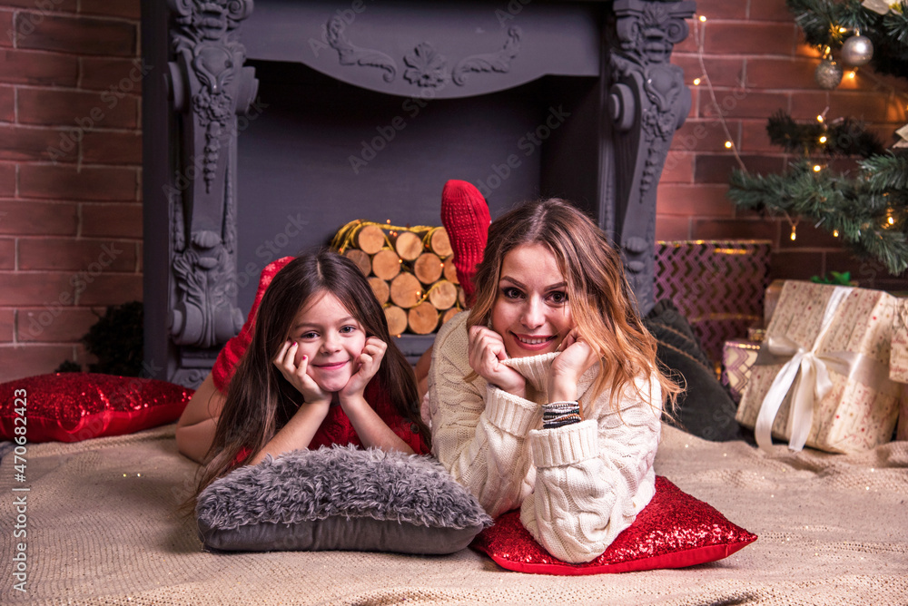 Young pretty mother with daughter lying near the Christmas tree in front of the fireplaceю (New Year, 2022, Christmas concept)