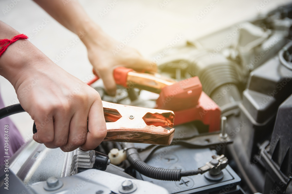 Asian young woman charging a car battery from the other car by using battery connector jump between battery. Asian young woman charging a car battery from the other car by using battery connector jump between battery.