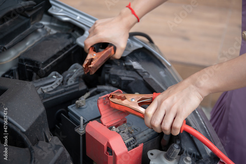 Asian young woman charging a car battery from the other car by using battery connector jump between battery.