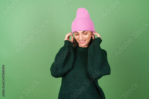 Young woman on a green background in a warm cozy sweater and a pink hat cute smiling