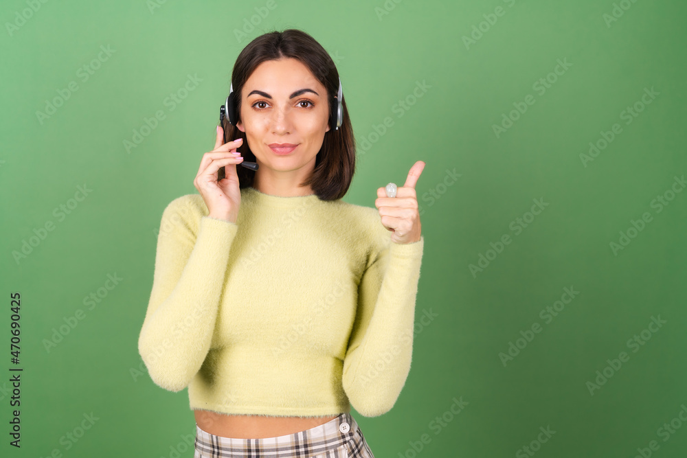 Young woman on a green background in a yellow sweater and a plaid skirt, manager, support worker, salesperson, taking calls from customers with pleasure