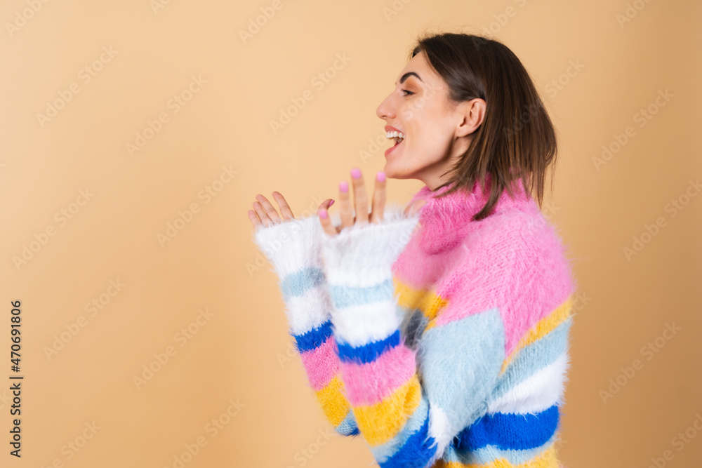 A young woman on a beige background in a bright multi-colored cozy knitted sweater is excited, surprised, shocked A young woman on a beige background in a bright multi-colored cozy knitted sweater is excited, surprised, shocked