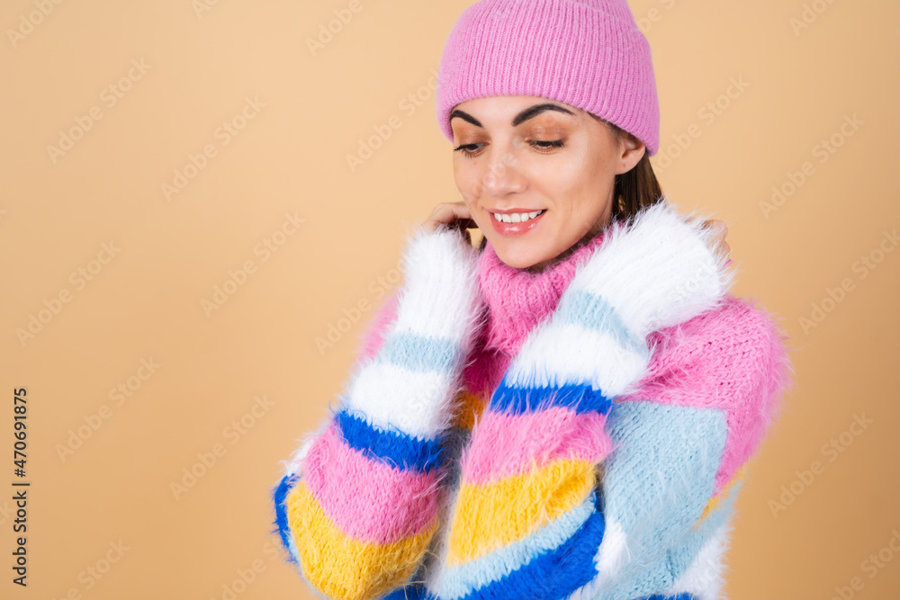 Young woman on a beige background in a bright multi-colored cozy knitted sweater and a hat comfortably hugs herself, warmth and comfort Young woman on a beige background in a bright multi-colored cozy knitted sweater and a hat comfortably hugs herself, warmth and comfort
