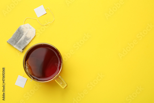 Tea bags and glass cup of hot drink on yellow background, flat lay. Space for text photo