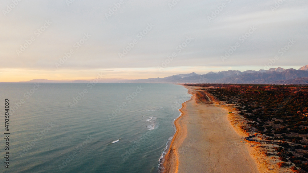 Aerial view of Ligurian sea, sandy shore and The Apuan Alps mountain range at sunset. Beautiful light and airy bird's eye view landscape in Tuscany region, Italy. Drone photography.