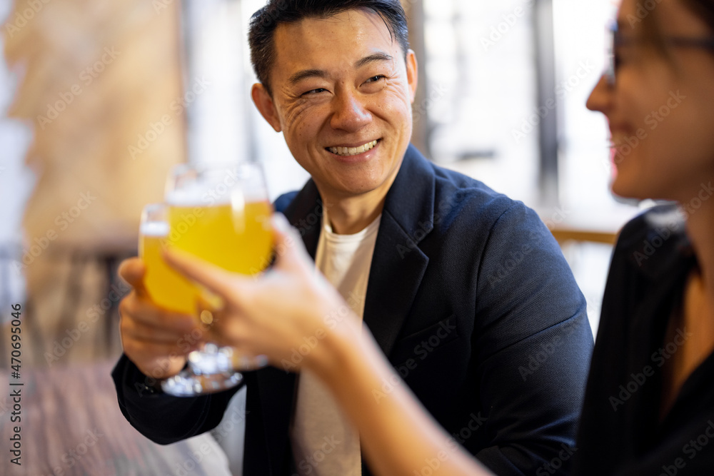 Multiracial friends or business partners talking and drinking beer in modern pub. Concept of rest and leisure. Business deal while drinking at the bar. Pleased young european woman and adult asian man Multiracial friends or business partners talking and drinking beer in modern pub. Concept of rest and leisure. Business deal while drinking at the bar. Pleased young european woman and adult asian man