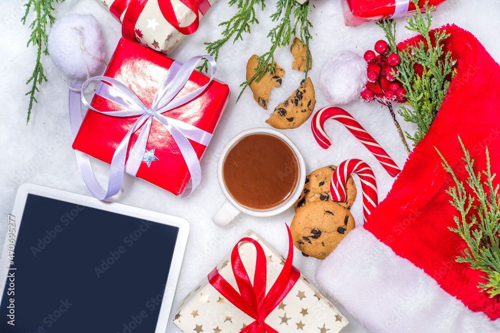 Creative layout frame with lot gift boxes, christmas tree branches, pine cones, hot chocolate mug, xmas sweet, tablet pc on white fluffy fur background. Xmas and New Year preparation background Creative layout frame with lot gift boxes, christmas tree branches, pine cones, hot chocolate mug, xmas sweet, tablet pc on white fluffy fur background. Xmas and New Year preparation background