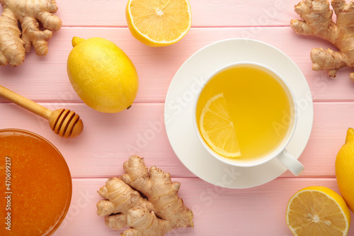 Ginger tea with lemon in a white cup on pink wooden background.