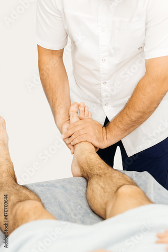 Osteopath working with ankle, examines a man's foot
