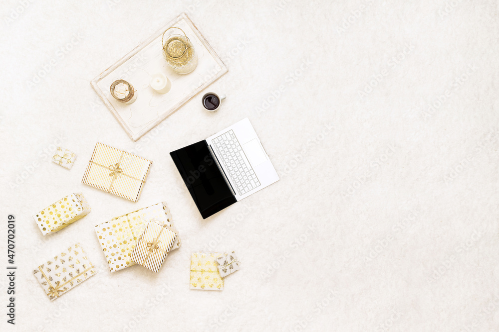 Fototapeta premium Christmas. Online shopping. Laptop among the many wrapped gifts in white gold wrapping paper on the snow white carpet . Top view. Concept