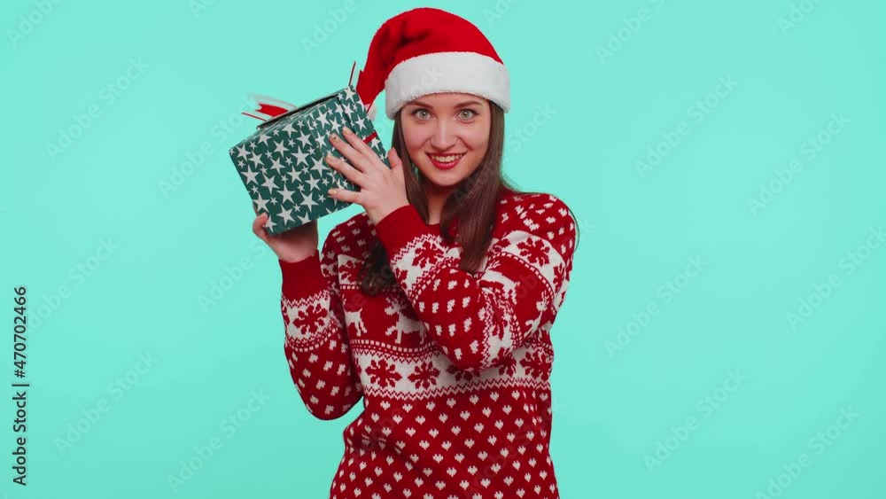 Funny adult girl 20s years old wears red deer New Year sweater holding gift, received present and interested in what inside box on blue background studio. Happy Christmas holiday celebration eve party Funny adult girl 20s years old wears red deer New Year sweater holding gift, received present and interested in what inside box on blue background studio. Happy Christmas holiday celebration eve party