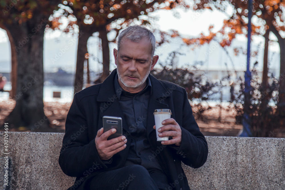 man sitting chatting with mobile phone while having coffee on autumn background man sitting chatting with mobile phone while having coffee on autumn background