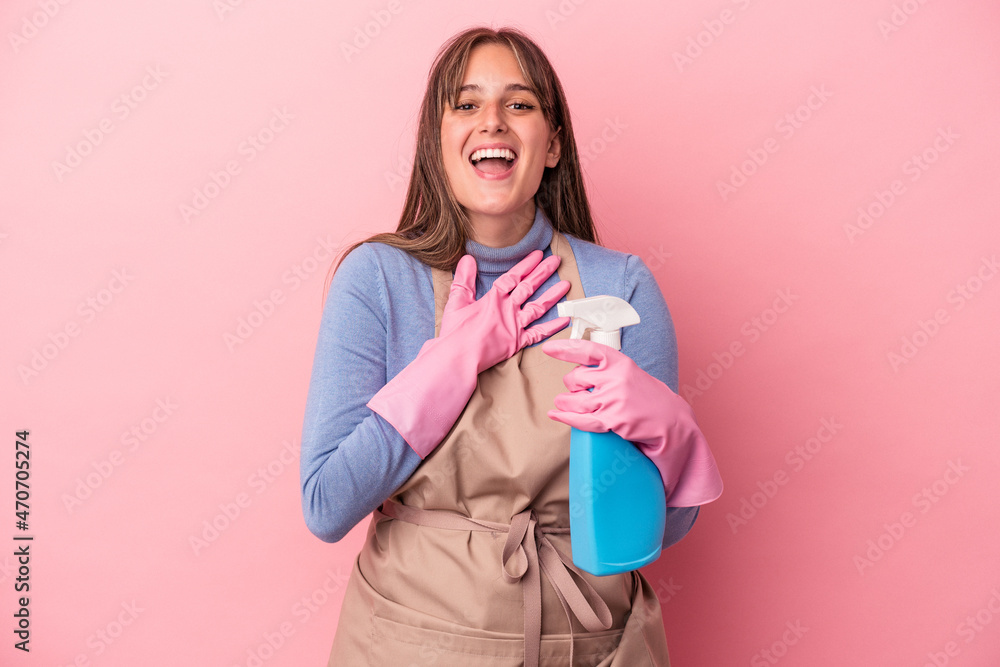 Young caucasian cleaner woman holding spray isolated on pink background laughs out loudly keeping hand on chest. Young caucasian cleaner woman holding spray isolated on pink background laughs out loudly keeping hand on chest.