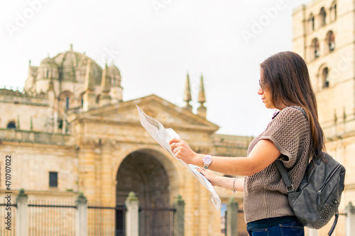 Young caucasian woman using a map with the medieval cathedral of zamora in the background.