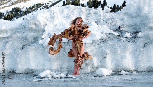 Young sexy blonde naked woman in winter, stylishly hidden by creative, dry, dried banana tree stands in the snow, freezes, accusing the world of climate change