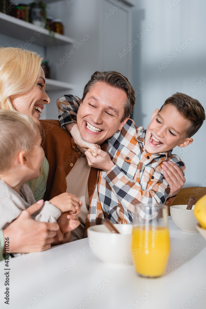 joyful family having fun during breakfast near bowls and orange juice on kitchen table joyful family having fun during breakfast near bowls and orange juice on kitchen table