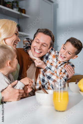 joyful family having fun during breakfast near bowls and orange juice on kitchen table