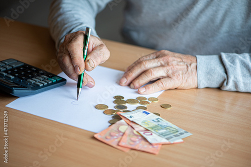 Hands of old senior man with calculator and bills counting euro money at home.