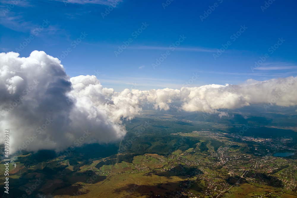 Aerial view from airplane window at high altitude of distant city covered with puffy cumulus clouds forming before rainstorm.